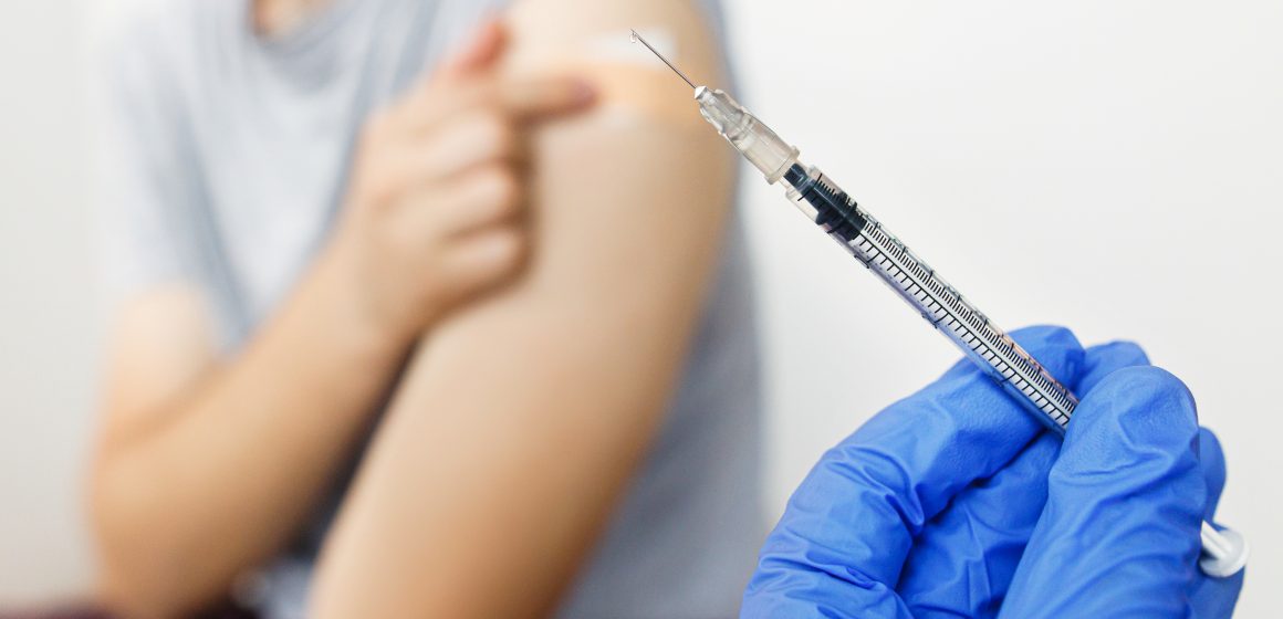 Syringe with vaccine in doctor hand on background of man with co Quase metade da população vacinada