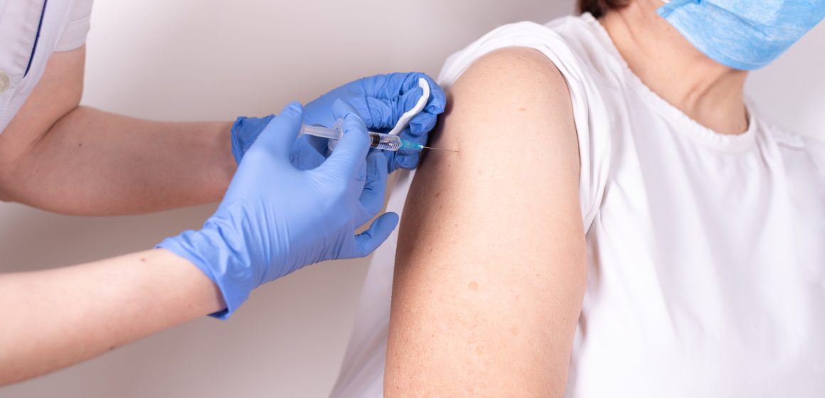 Gloved hands injectng a syringe with covid-19 vaccine into the shoulder of an old woman. Covid-19: Isolamento e Auto-Cuidados